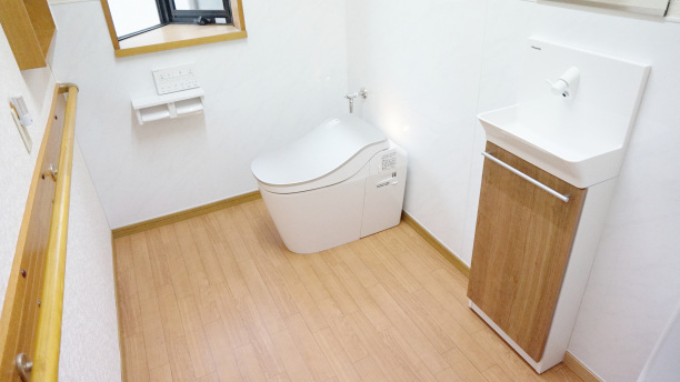 同系色でまとまった床、手すり、手洗い器とシルバー色の便座蓋のトイレ